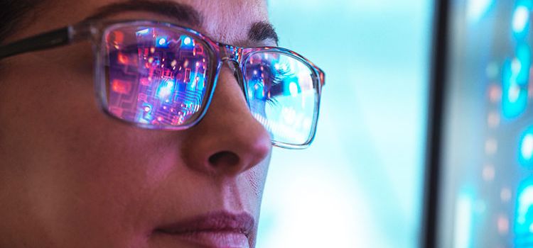 Junge Frau beim Betrachten eines Monitors mit Daten, die sich in ihrer Brille spiegeln